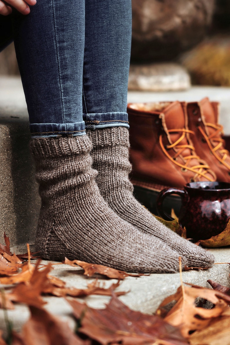 Woman wearing a pair of The Beginner Socks that were knitted using brown worsted-weight yarn. These knitted socks are thick, warm, and cozy, and the knitting pattern is easy to follow and great for beginner knitters to knit a pair of socks.