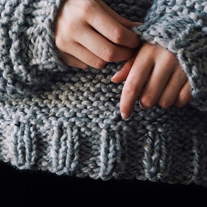 May include: A chunky knit sweater in a heathered grey yarn featuring a thick garter stitch texture throughout the body and a ribbed hemline at the waist. The garment has long sleeves with ribbed cuffs and a visible DarlingJadore watermark.
