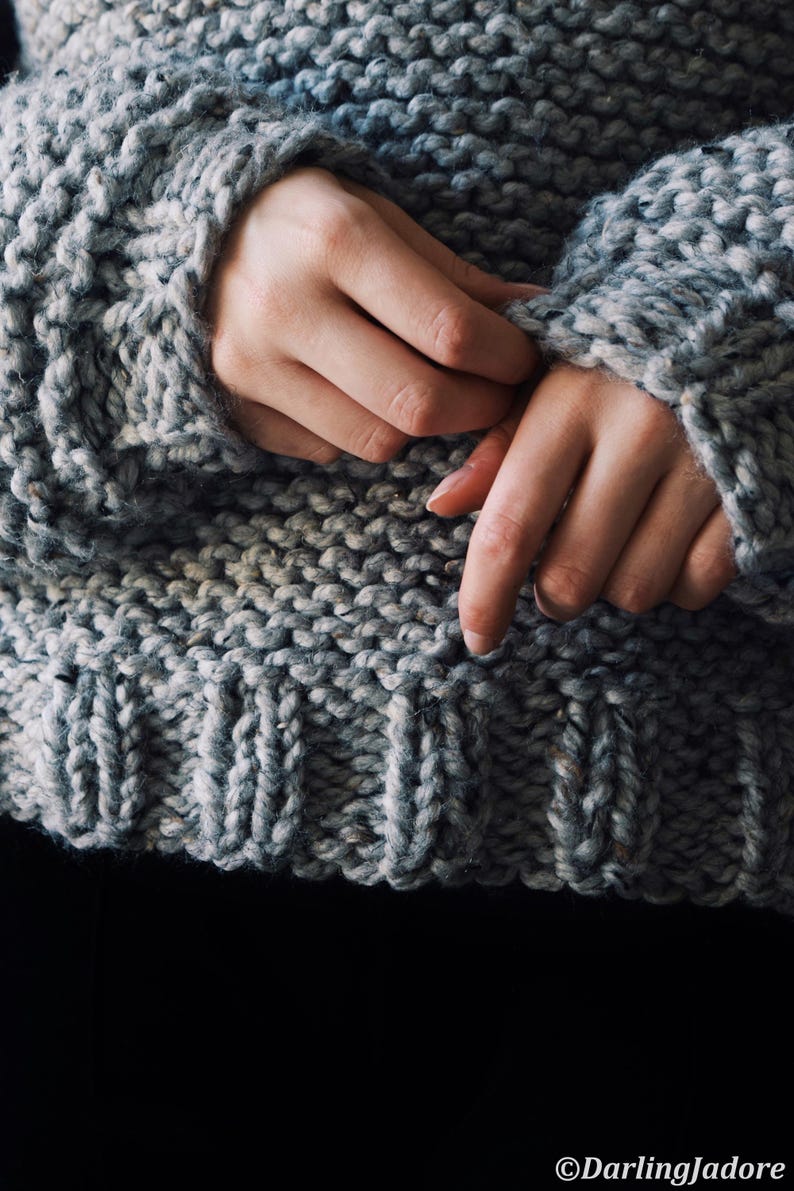 May include: A chunky knit sweater in a heathered grey yarn featuring a thick garter stitch texture throughout the body and a ribbed hemline at the waist. The garment has long sleeves with ribbed cuffs and a visible DarlingJadore watermark.