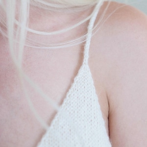 Knit camisole single knitting pattern. v-neck tank top knitting pattern. beginner knit singlet pattern. summer tank top knitting pattern with spaghetti straps. Easy cami knit pattern. Summer singlet top knitting pattern. Knitted singlet. Woman wears a basic knitted camisole that was knit in white yarn using this knitting pattern