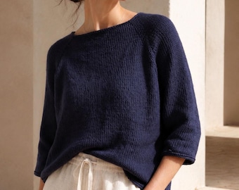 Puede incluir: Un suéter de punto azul marino con escote ancho y mangas tres cuartos, combinado con pantalones de color blanco roto con cintura elástica y cordón ajustable. El suéter presenta un patrón de punto texturizado y un corte holgado.