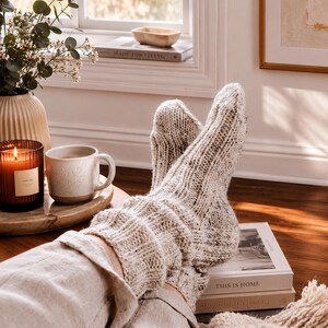 May include: A pair of thick, cream-colored knit socks with subtle dark flecks throughout. The socks feature a ribbed texture that extends from the cuff down to the foot, providing a chunky, cozy appearance. The material appears to be a wool blend.