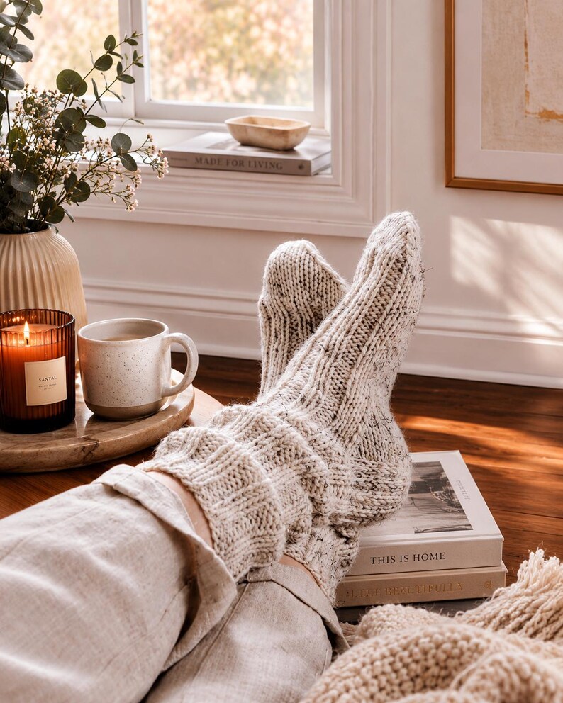 May include: A pair of thick, cream-colored knit socks with subtle dark flecks throughout. The socks feature a ribbed texture that extends from the cuff down to the foot, providing a chunky, cozy appearance. The material appears to be a wool blend.