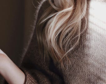 May include: A long-sleeved, chunky knit sweater in a solid medium brown color. The garment features a ribbed crew neckline and ribbed cuffs at the wrists. The knit texture is visible throughout the fabric, which has a soft, slightly fuzzy appearance.
