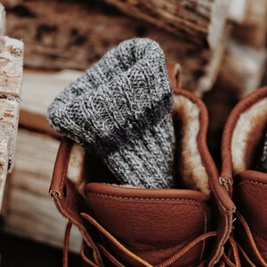 Closeup photo of a pair of knitted socks, The Camp Socks, in a pair of boots. These cozy boot socks are knitted in grey yarn and these knit socks look warm and great to wear in boots or while hiking.
[boot socks knit pattern, knit socks pattern]