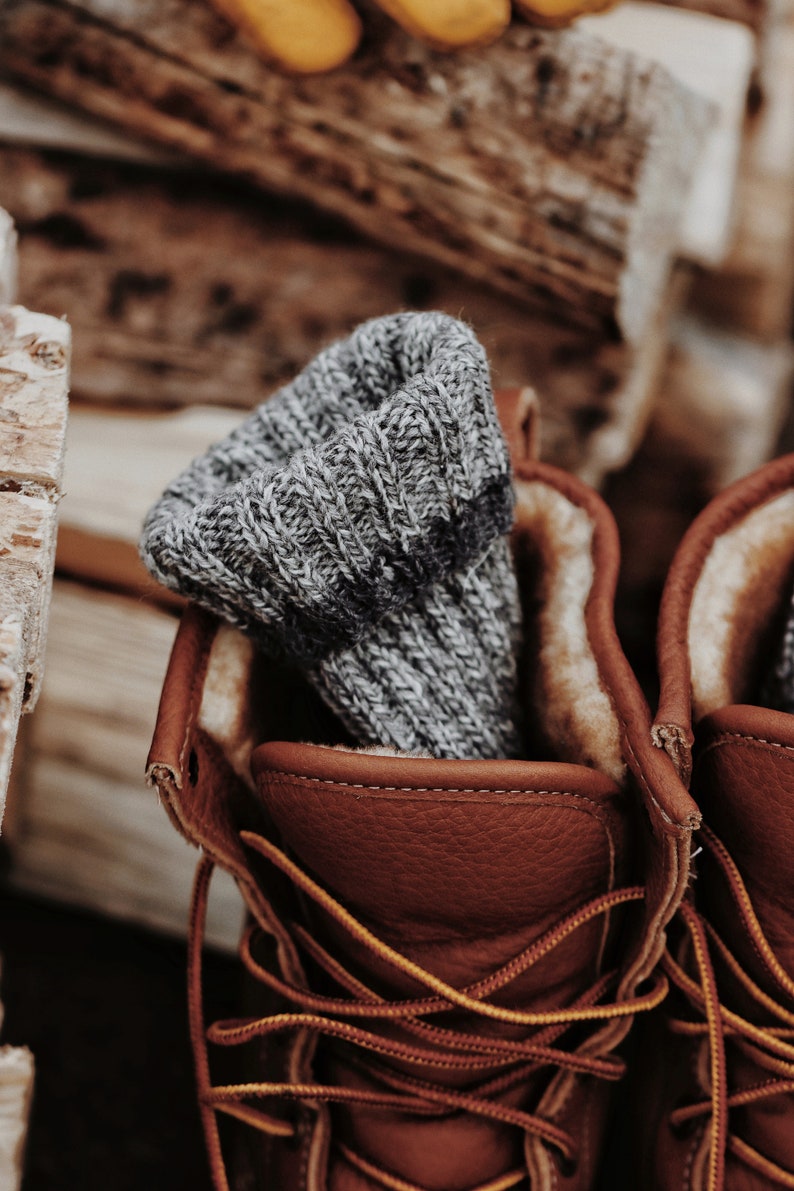 Closeup photo of a pair of knitted socks, The Camp Socks, in a pair of boots. These cozy boot socks are knitted in grey yarn and these knit socks look warm and great to wear in boots or while hiking.
[boot socks knit pattern, knit socks pattern]