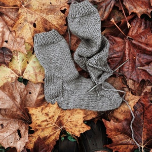 A pair of knitted socks are laying on fall leaves. These socks are knitted using a brown worsted-weight yarn. This easy knitting pattern is a great way to knit a pair of easy socks for beginners knitters.
[socks knit pattern, knitted socks]