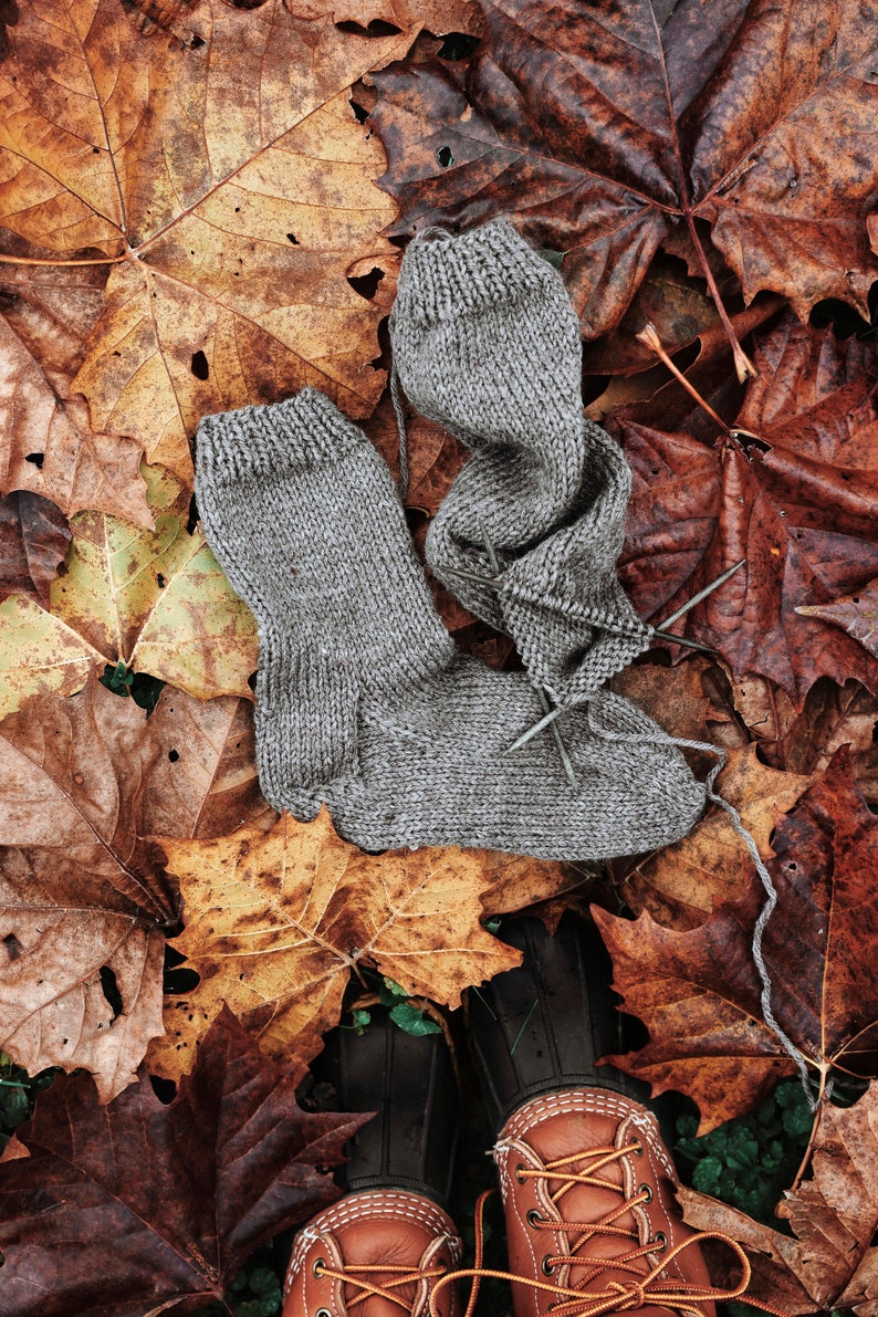 A pair of knitted socks are laying on fall leaves. These socks are knitted using a brown worsted-weight yarn. This easy knitting pattern is a great way to knit a pair of easy socks for beginners knitters.
[socks knit pattern, knitted socks]