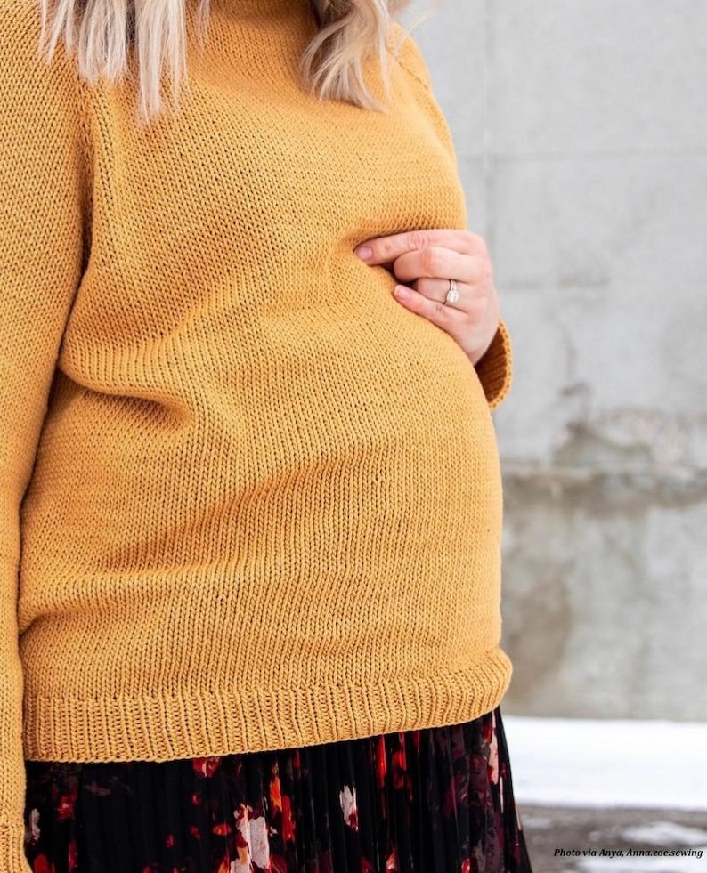 A pregnant woman wears a yellow knitted sweater, The Weekend Sweater, using this knitting pattern. The knit jumper looks comfortable and cozy, featuring simple knit stitches (Stockinette) and ribbing details. 
[sweater knit pattern, raglan pattern]