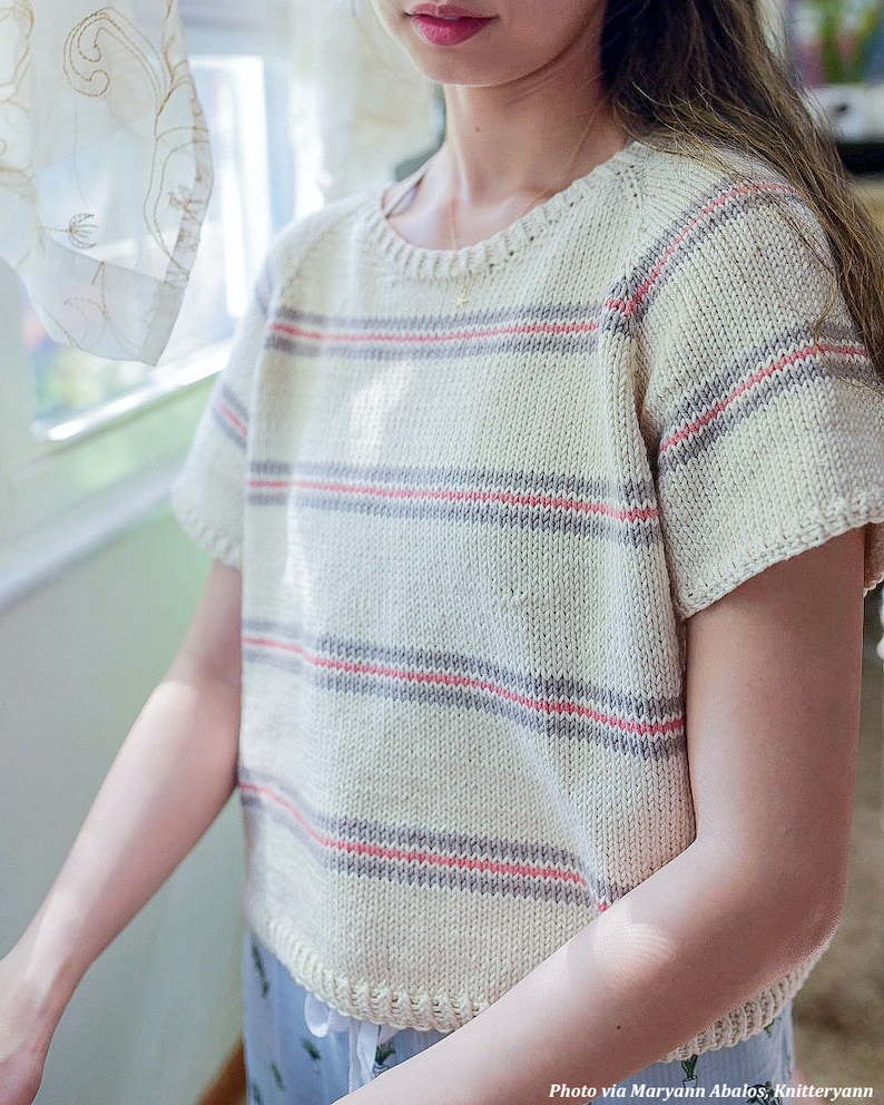 Woman wears a basic knit tee shirt, The Classic Tee, in cream with stripes. This simple knitted tshirt looks lightweight and great as a summer top. This easy tshirt features ribbing and classic knit stitches.
[sweater knitting patterns, easy knit]