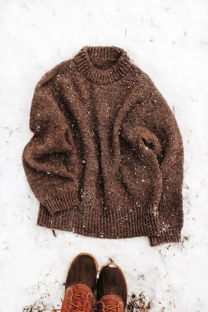 A top-down raglan knitted sweater, The Weekend Sweater, is laying on the slow. The sweater was knitted in cozy worsted weight brown yarn, and the knitting pattern for this knit pullover features a double-knit neck and ribbing on the sleeve cuffs.