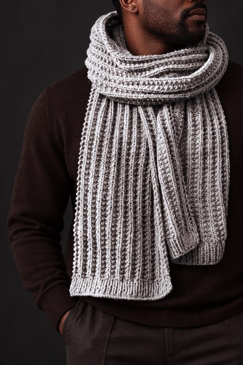 May include: A light gray knitted scarf featuring a prominent vertical ribbed texture. The scarf is wrapped around the neck and hangs down in long, straight sections, showcasing a consistent, thick yarn construction with a defined border at the ends.