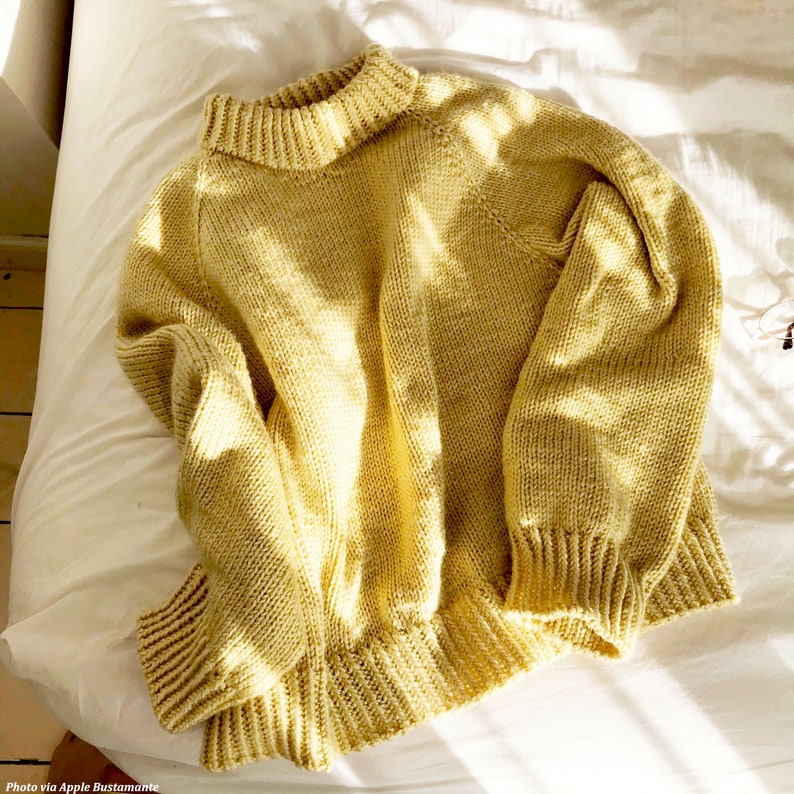 The Weekend Sweater is knitted in yellow laying on a bed. The knitting pattern for this sweater features easy knit stitches and a double-knit collar. This cozy jumper sweater is fun to knit and makes a great knit pullover to wear. [knit jumpers, knit