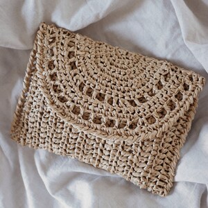 A raffia clutch that was crocheted using this crochet pattern is laying flat. The details on this summer crochet purse bag includes some lace and simple crochet stitches. 
[raffia clutch crochet pattern, easy bag crochet pattern, purse crochet]