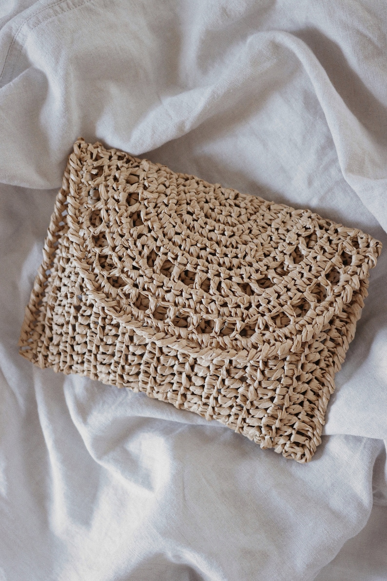 A raffia clutch that was crocheted using this crochet pattern is laying flat. The details on this summer crochet purse bag includes some lace and simple crochet stitches. 
[raffia clutch crochet pattern, easy bag crochet pattern, purse crochet]