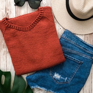 A basic knitted tee shirt is knit in red yarn and is laid flat next to jeans and summer clothing. The Classic Tee knitting pattern features a crew neck and simple stitches making it easy to knit. 
[sweater knit patterns, knit raglan patterns]