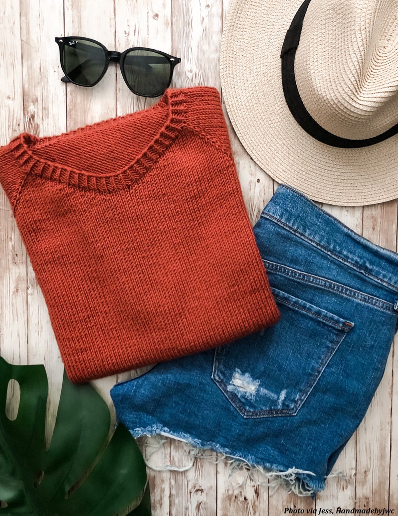 A basic knitted tee shirt is knit in red yarn and is laid flat next to jeans and summer clothing. The Classic Tee knitting pattern features a crew neck and simple stitches making it easy to knit. 
[sweater knit patterns, knit raglan patterns]