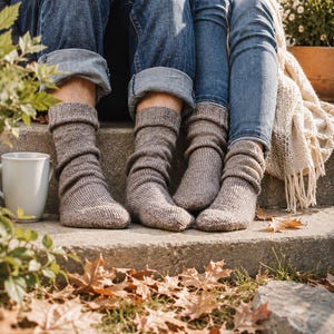 Könnte beinhalten: Zwei Paar wadenlange, hellbraune Strickstrümpfe mit geripptem Bündchen. Die Socken haben eine strukturierte, wolle-ähnliche Optik und werden an den Füßen getragen, wobei sie über den Knöchel reichen und eine einfache, funktionale Strickweise aufweisen.