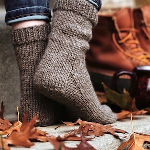 Woman wears The Beginner Socks that were knit using the knitting pattern. These easy knit socks were knitted in brown yarn using worsted weight yarn, and these knit socks are easy to make, cozy, and warm. 
[socks knit pattern, easy knit sock pattern]