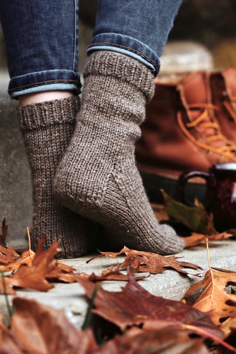 Woman wears The Beginner Socks that were knit using the knitting pattern. These easy knit socks were knitted in brown yarn using worsted weight yarn, and these knit socks are easy to make, cozy, and warm. 
[socks knit pattern, easy knit sock pattern]