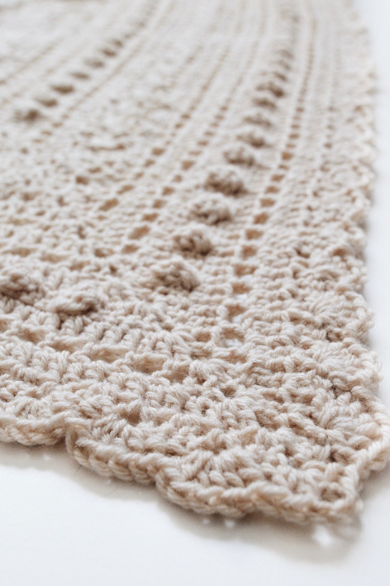 Closeup photo of a crocheted scarf, The Isla Scarf, which features lace and bobbles. This cozy triangle shawl is crocheted in cream yarn. [triangle crochet scarf, bobble scarf crochet pattern, triangle shawl crochet patterns, beginner crochet]