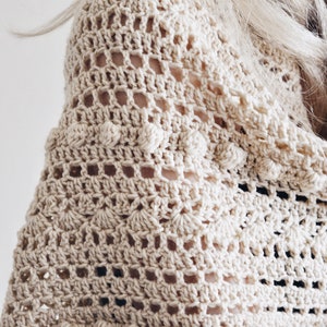Woman wears a bobble crochet shawl, The Isla Scarf, which was crocheted in cream yarn. This vintage-inspired crochet scarf features lave and bobbles.
[crochet bobble scarf, crochet triangle scarf, crochet shawl patterns, easy crochet shawl]