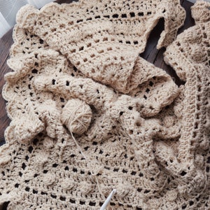 A crocheted shawl, The Isla Scarf, is laid flat and being crocheted in a cream yarn. [triangle shawl crochet pattern, bobble scarf crochet pattern, crochet bobble scarf pattern, bobble scarf crochet patterns, beginner crochet]