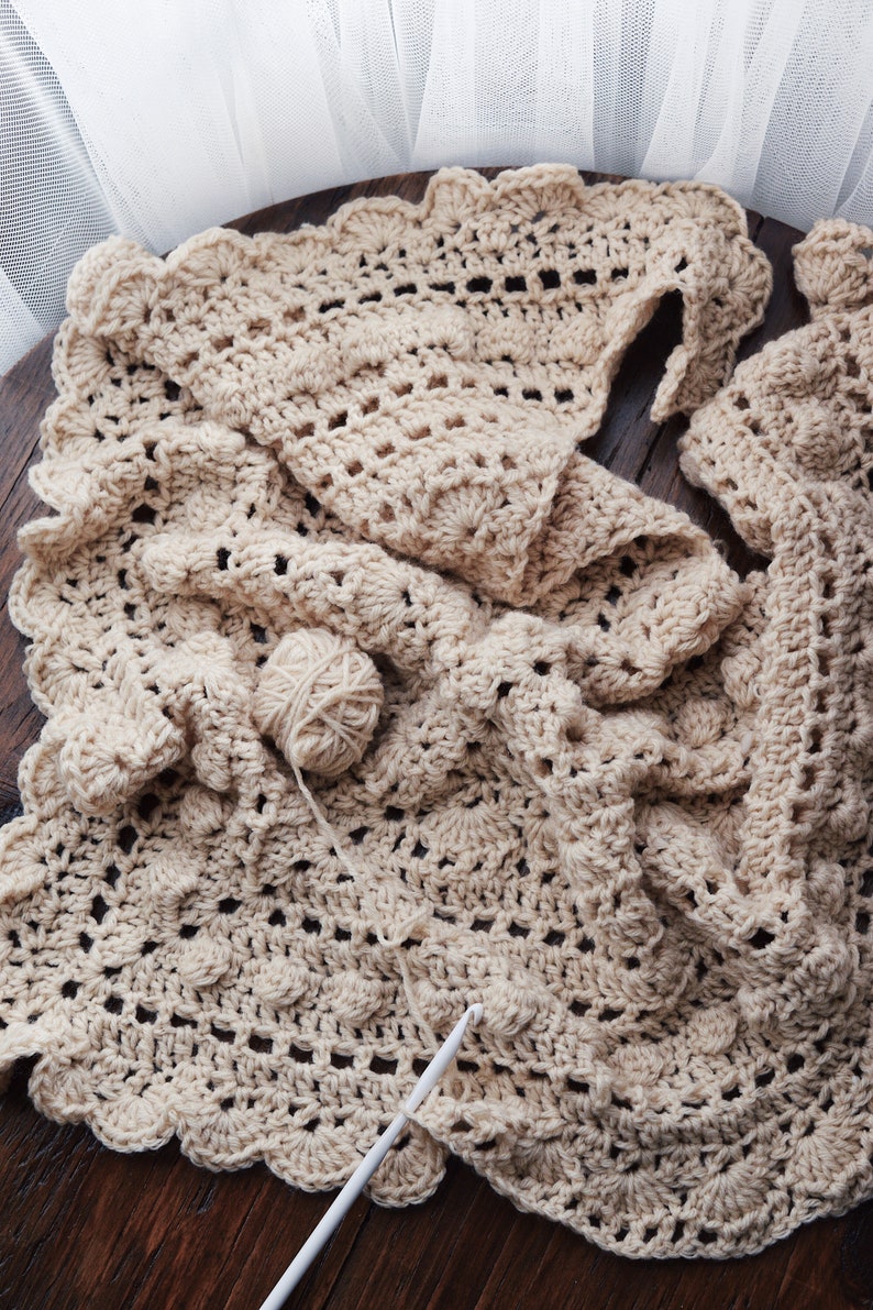 A crocheted shawl, The Isla Scarf, is laid flat and being crocheted in a cream yarn. [triangle shawl crochet pattern, bobble scarf crochet pattern, crochet bobble scarf pattern, bobble scarf crochet patterns, beginner crochet]