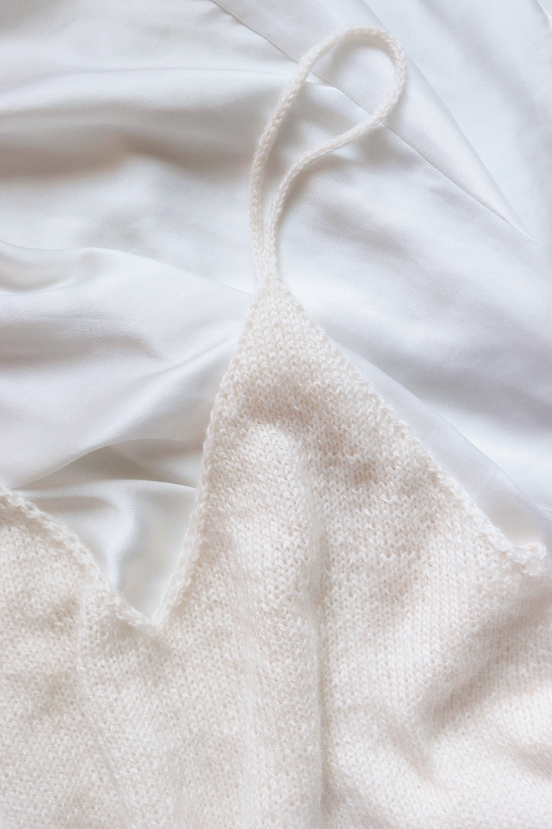 The Classic Camisole is knitted in cream yarn using this knitting pattern and and is laid flat. The spaghetti straps of this cami tank top are shown, along with a v-neck design and simple knit stitches, making it a lightweight easy camisole to knit.