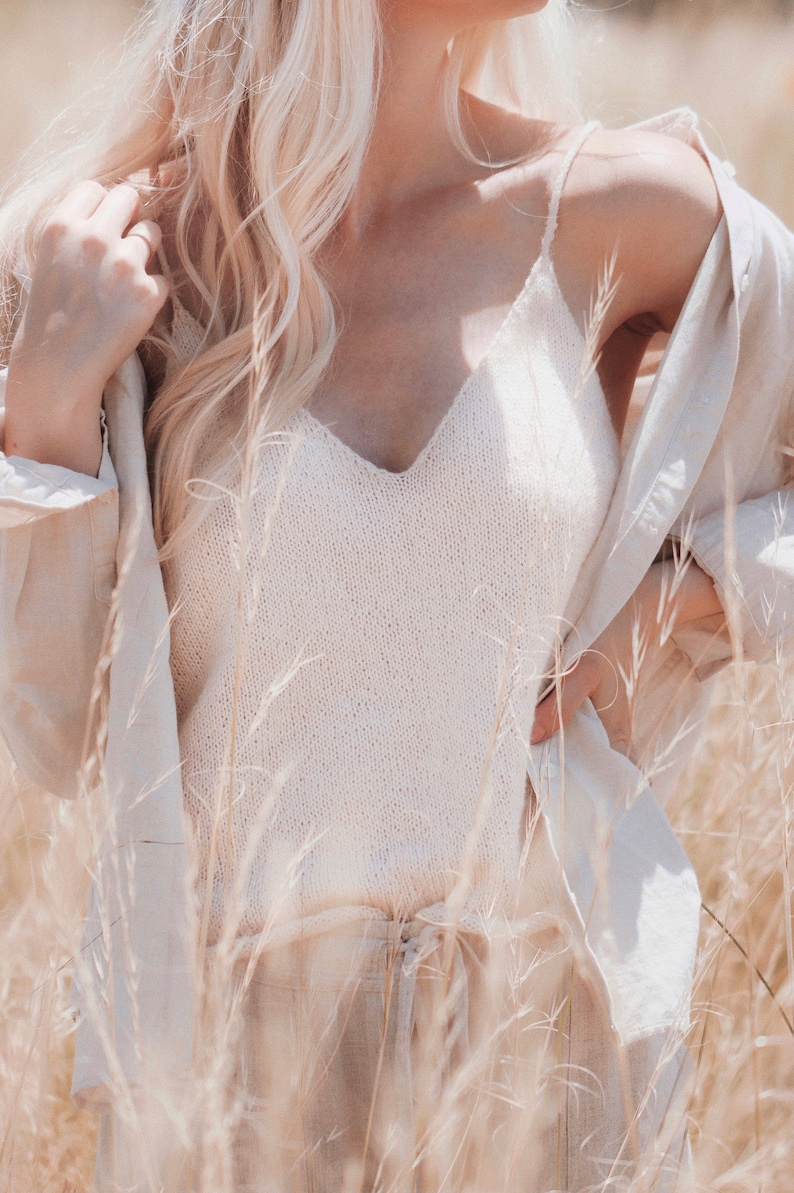 Woman wears The Classic Camisole that was knitted in white yarn using this knitting pattern. The thin spaghetti straps and v-neck of this cami tank top are features, and it looks like a lightweight camisole that's great for layering.