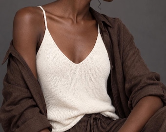 May include: A cream-colored knit camisole with thin spaghetti straps and a V-neckline, layered under a dark brown long-sleeved button-down shirt and paired with matching dark brown drawstring trousers made of a textured fabric.