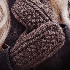 May include: A pair of dark brown knitted mittens featuring a prominent cable knit pattern on the back of the hand. The mittens are constructed with a thick, textured yarn and have a ribbed cuff design that extends slightly past the wrist area.