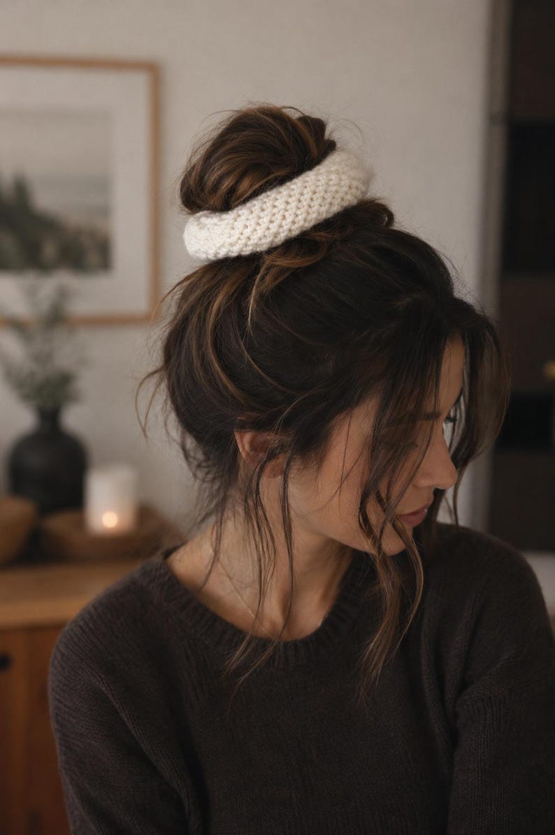 May include: A thick, off-white knitted hair scrunchie with a textured, ribbed surface. The accessory is circular in shape and features a dense, woven yarn construction, providing a soft and voluminous appearance for securing hair in a bun style.