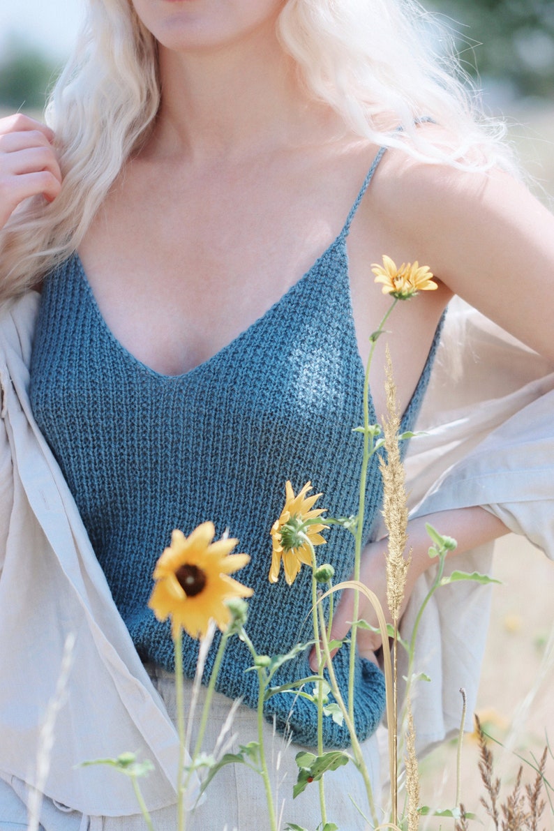 Woman wears blue knitted camisole tank top, The Bluebell Camisole knitting pattern. This knit cami is lightweight and features a v-neck and thin spaghetti straps. This knit tank top is great for summer and layering.
[knit patterns, knitting pattern]