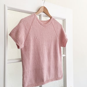 A knitted tshirt, The Classic Tee, is hanging on a door and knit using pink yarn. This basic knit shirt features a raglan construction and pretty knit stitches. This knit tee looks lightweight and comfortable for summer.
[easy knitting patterns]