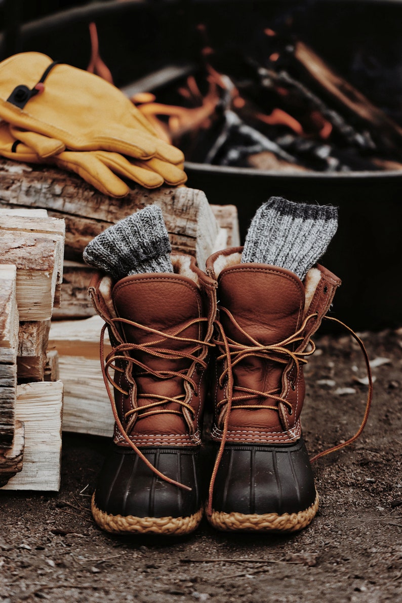 Knitted socks are inside winter hiking boots next to a fire. These knit socks, The Camp Socks, are warm and soft and look great to wear during fall or winter. 
[socks knitting pattern, knit sock patterns, easy knitting patterns, knit patterns]