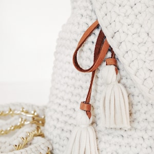 Close-up photo of The Lola Bag, a crochet backpack purse crochet pattern featuring cream yarn and tassels with metal hardware accents. 
[crochet pattern, easy crochet purse, purse crochet pattern, backpack purse crochet pattern, bag crochet pattern]