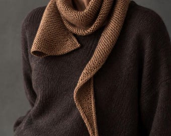 May include: A dark brown long-sleeved knit sweater paired with a light brown garter stitch knit scarf. The scarf features a tapered, pointed end and is wrapped around the neck. The sweater has a simple crew neckline and a textured knit construction.