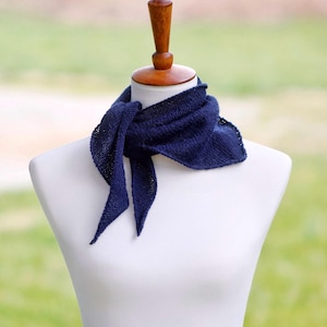 May include: A dark navy blue triangular scarf with a fine knit texture, tied around the neck of a white mannequin. The scarf features a simple garter stitch pattern and pointed ends that drape naturally, showcasing a solid, deep blue color throughout.