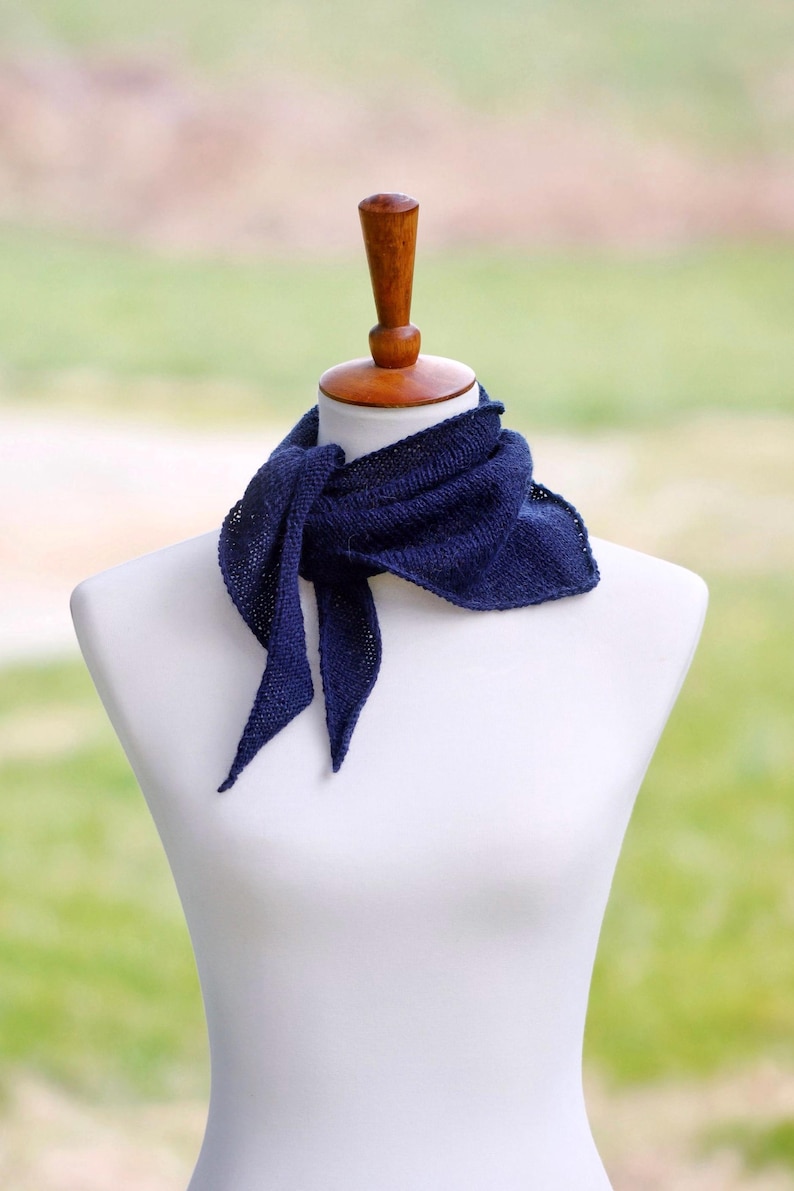 Puede incluir: Un pa&ntilde;uelo triangular de color azul marino oscuro con una textura de punto fino, atado alrededor del cuello de un maniqu&iacute; blanco. La bufanda presenta un patr&oacute;n de punto bobo simple y extremos puntiagudos que caen naturalmente, mostrando un color s&oacute;lido.