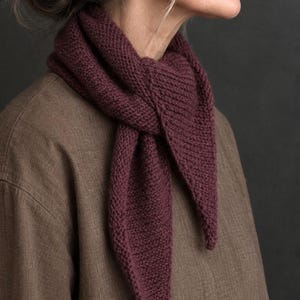 May include: A deep burgundy triangular scarf featuring a textured garter stitch knit pattern. The scarf is tied in a simple knot around the neck, with two pointed ends hanging down. The knit fabric has a consistent, dense, and uniform appearance.