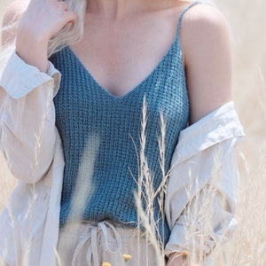 Woman wears a knit summer tank top, The Bluebell Camisole, knitted in blue yarn. This knit cami is lightweight and features a v-neck and thin straps. This stylish knit camisole is a great layering piece and cozy.
[knit patterns, easy knit pattern]