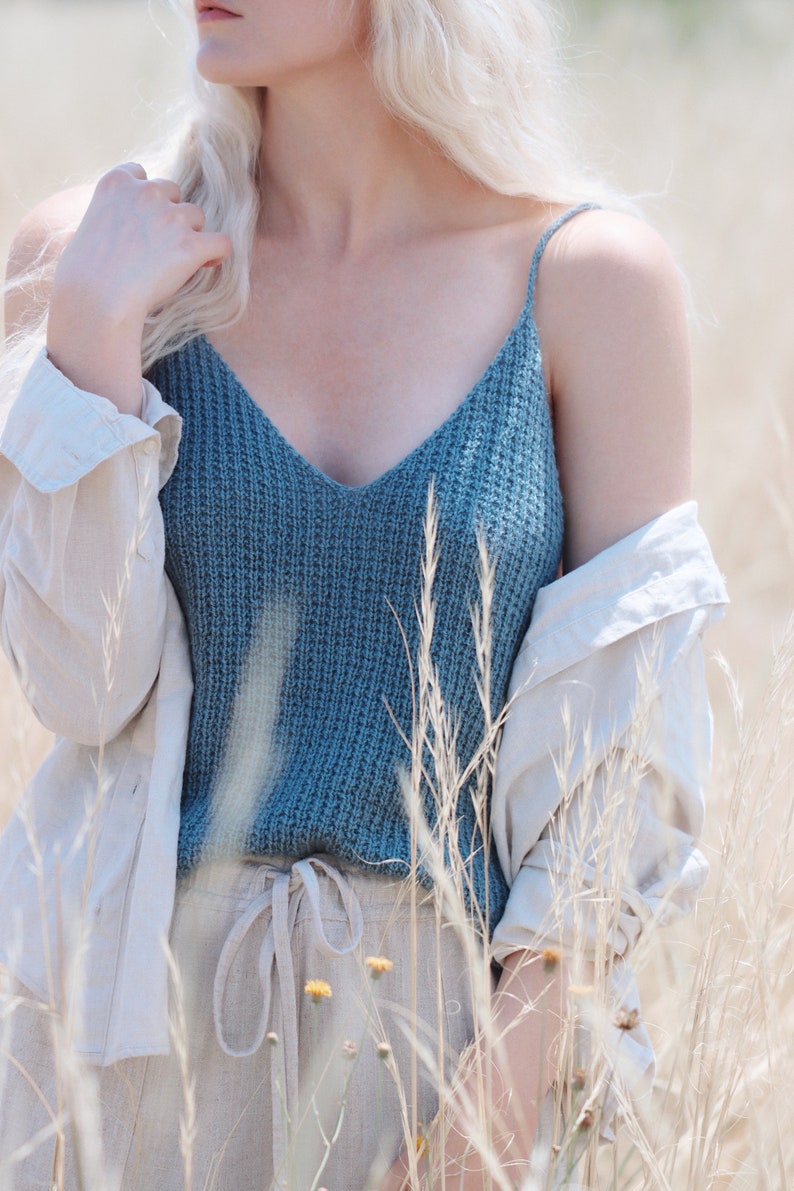 Woman wears a knit summer tank top, The Bluebell Camisole, knitted in blue yarn. This knit cami is lightweight and features a v-neck and thin straps. This stylish knit camisole is a great layering piece and cozy.
[knit patterns, easy knit pattern]