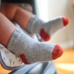 May include: A pair of grey baby socks with orange accents. The socks are knitted and have a soft, comfortable texture.