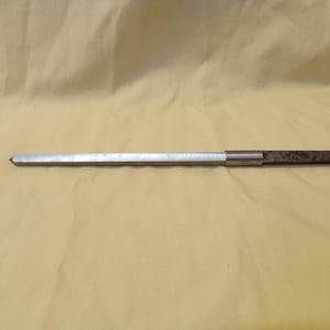 May include: A metal reamer tool with a silver shaft and a textured, dark brown handle. The reamer has a tapered, pointed end. The tool is designed for enlarging or shaping holes.