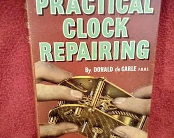 Puede incluir: Un libro de tapa dura titulado Practical Clock Repairing de Donald de Carle. La cubierta marrón presenta texto en verde claro y una ilustración de manos trabajando en un mecanismo de reloj de latón. El texto incluye With over 400 specially drawn illustrations.
