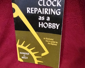 Puede incluir: Un libro de bolsillo titulado Clock Repairing as a Hobby de Harold C. Kelly. La portada presenta una sección superior negra con texto blanco y una sección inferior de color verde oliva oscuro con un gráfico amarillo de un engranaje.