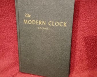 Puede incluir: Un libro de tapa dura negro titulado The Modern Clock de Goodrich. La portada presenta un acabado texturizado con el título y el nombre del autor impresos en letras doradas. El libro está colocado verticalmente, mostrando el diseño de la portada.