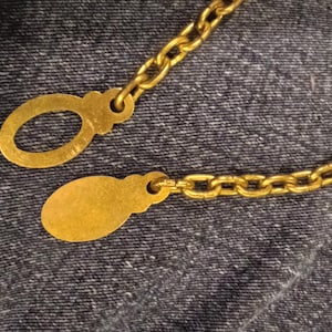 May include: A gold chain with two oval-shaped charms. The charms are smooth and have a shiny finish.