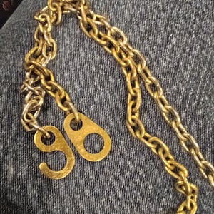 May include: A gold chain necklace with two metal tags that say "98" on them.